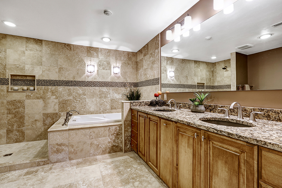 luxury bathroom interior with tile floor. bath tub with brown granite tile trim and vanity cabinet with large mirror.